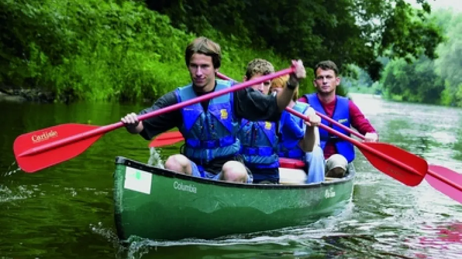 Vier junge Leute sitzen in einem kleinen Boot und paddeln auf einem Fluss.